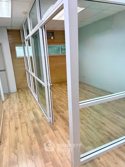 Modern office space with glass partitions and wooden flooring, ideal for professional settings.