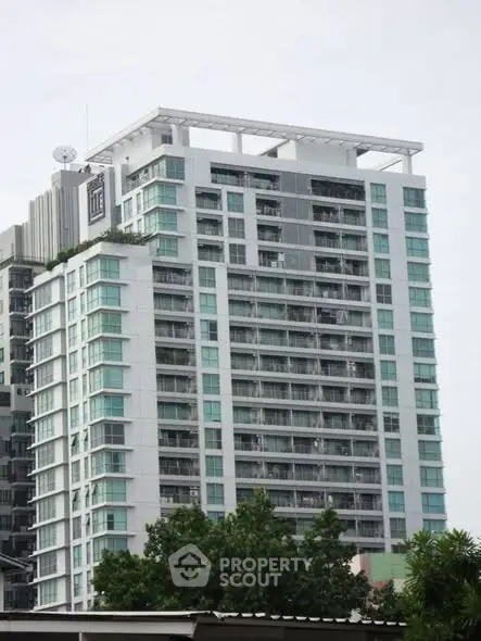 Modern high-rise building with glass balconies and lush greenery in urban setting.