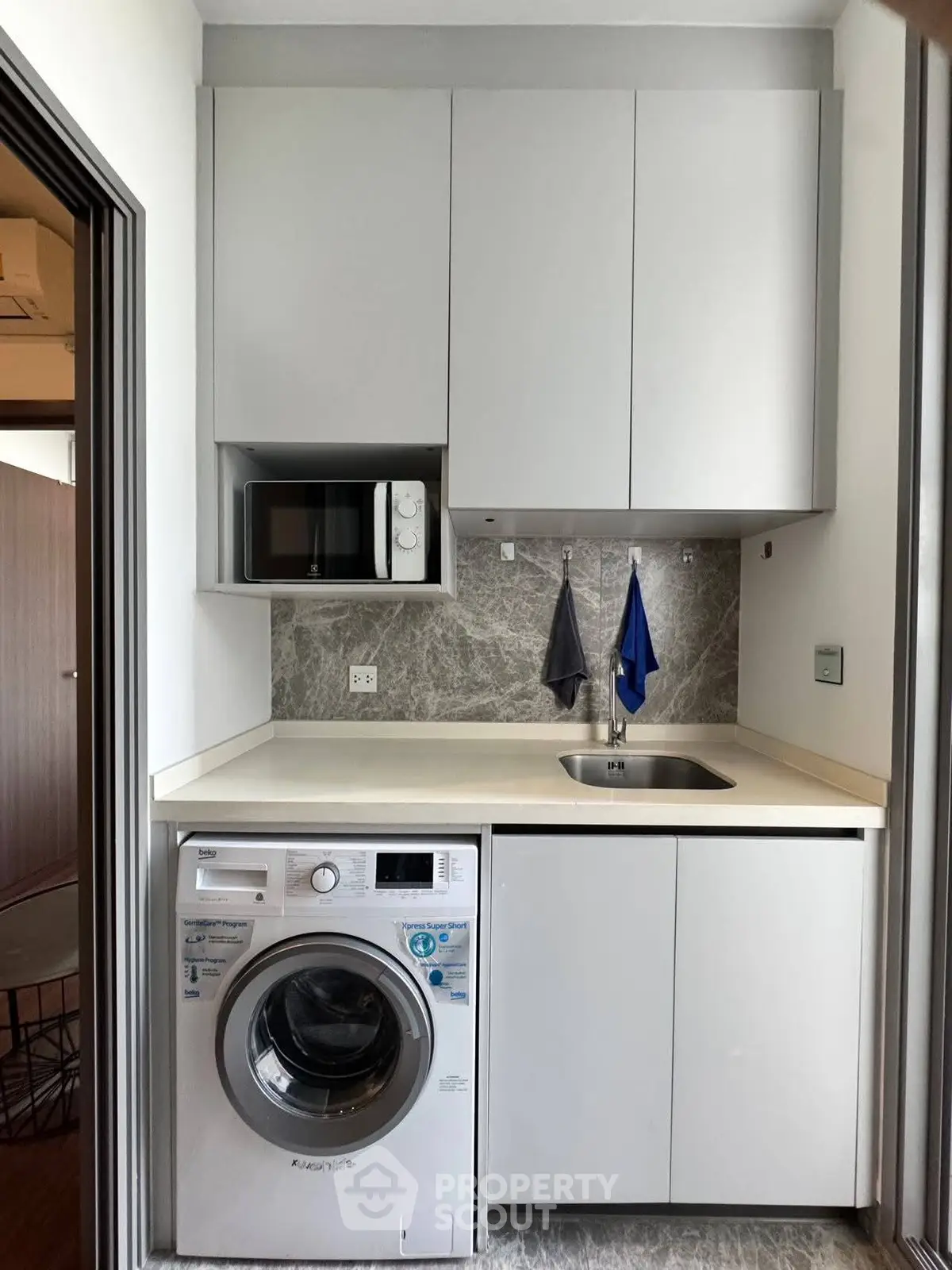 Compact laundry area with washing machine and microwave in modern apartment