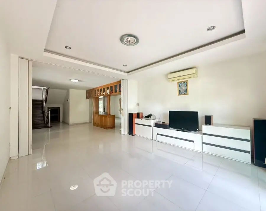 Spacious modern living room with sleek white tiles and built-in entertainment center.