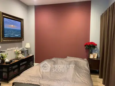 Cozy bedroom with elegant decor, featuring a framed seascape painting and a bouquet of red roses.