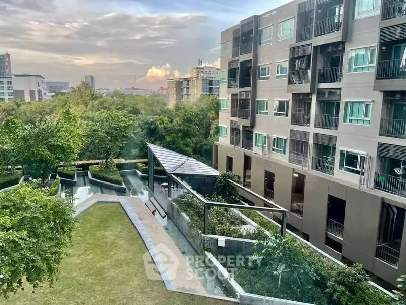 Modern apartment building with lush garden and scenic city view at sunset.