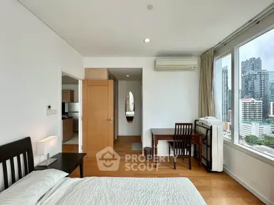 Spacious bedroom with city view, wooden flooring, and modern furnishings in a high-rise apartment.