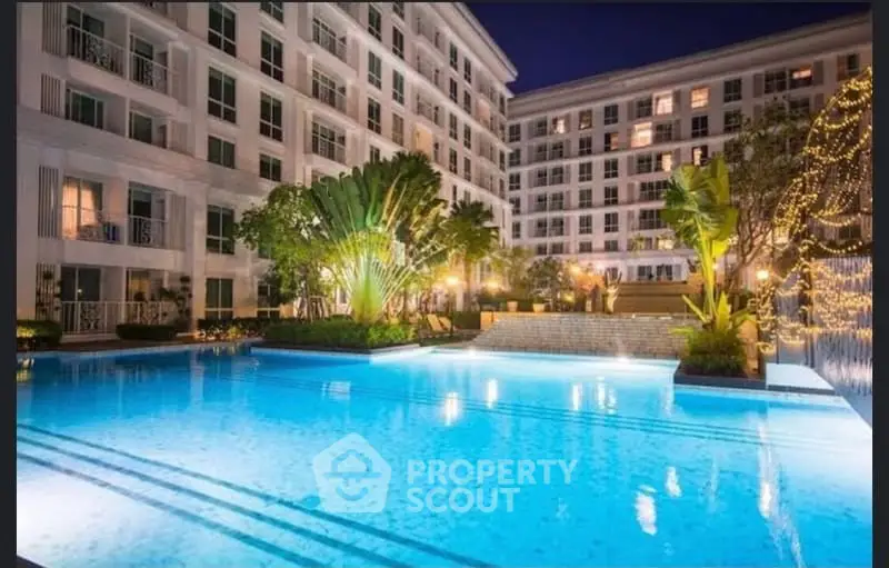 Luxurious apartment complex with illuminated pool and lush greenery at night.