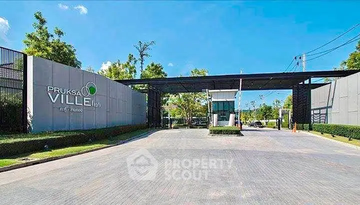 Modern gated entrance of Pruksa Ville with lush greenery and clear blue sky.