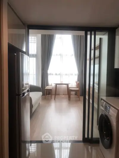 Modern apartment with open layout featuring kitchen and living area, large windows, and sleek appliances.