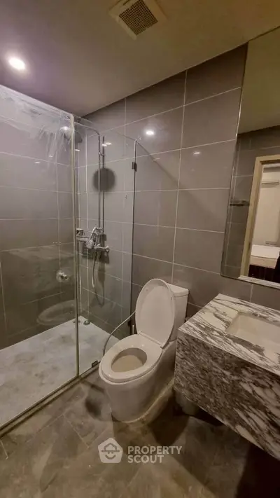 Modern bathroom with glass shower and marble sink in sleek apartment.