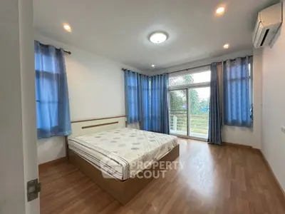 Spacious bedroom with large windows and blue curtains, featuring a comfortable bed and wooden flooring.