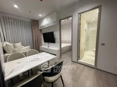 Modern apartment interior with open living and dining area, featuring sleek furniture and a view into the bedroom.
