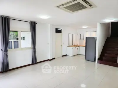 Spacious open-plan living area with modern kitchen and staircase, featuring sleek tile flooring and ample natural light.