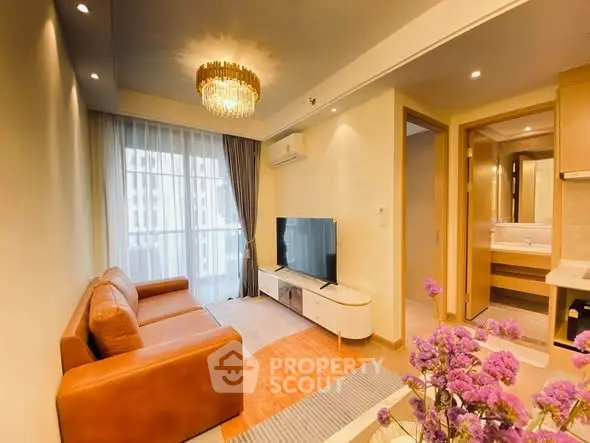 Modern living room with leather sofa, TV, and elegant chandelier in a stylish apartment.