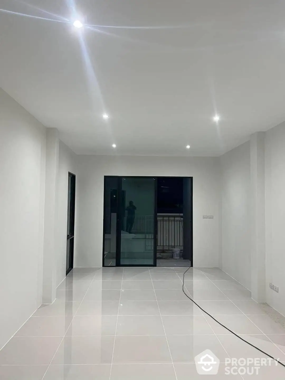 Spacious and modern living area with glossy white tiles, recessed lighting, and large sliding glass doors leading to a balcony, offering a blank canvas for personalization.