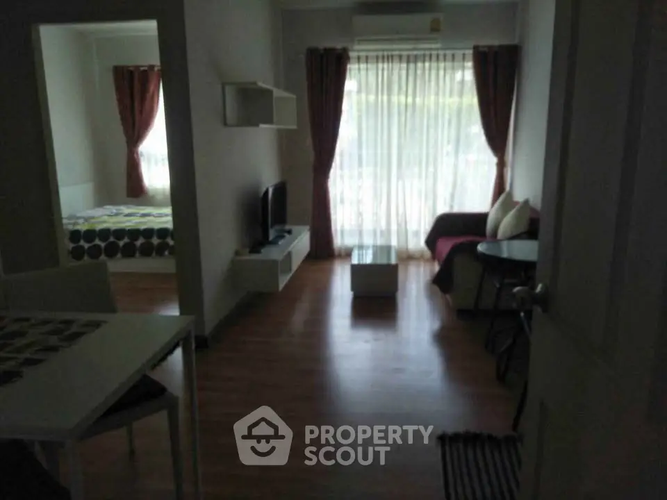 Cozy living room with natural light and view into bedroom, featuring modern decor and wooden flooring.