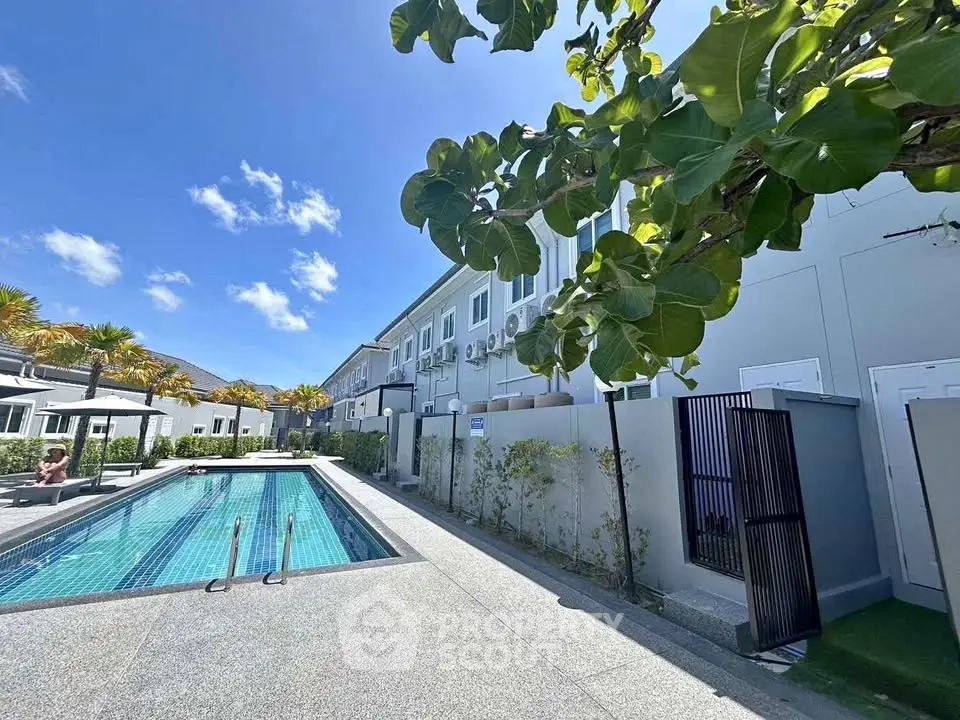 Modern residential complex with swimming pool and lush greenery under a clear blue sky.