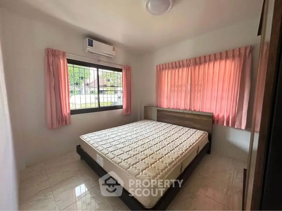Cozy bedroom with natural light and air conditioning, featuring pink curtains and a comfortable mattress.