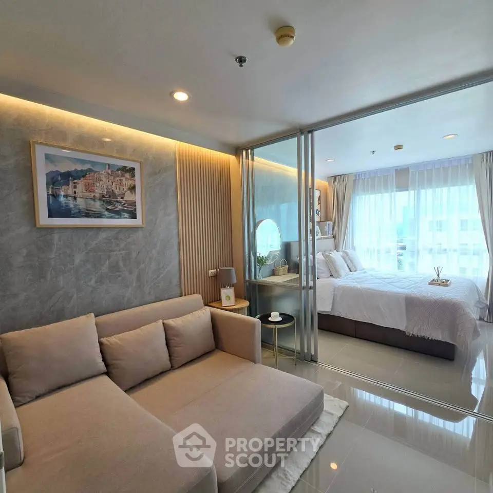 Modern studio apartment with cozy living area and bright bedroom separated by glass partition.