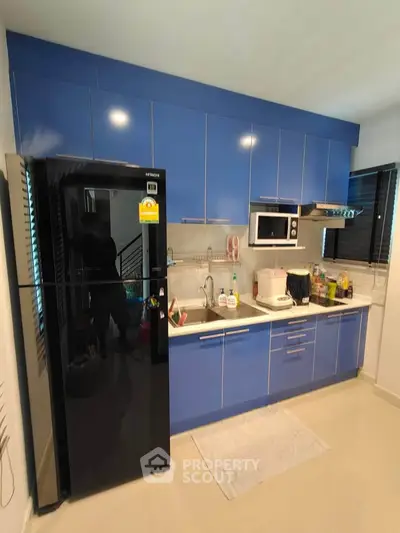Modern kitchen with blue cabinets and sleek appliances, featuring a black fridge and microwave.