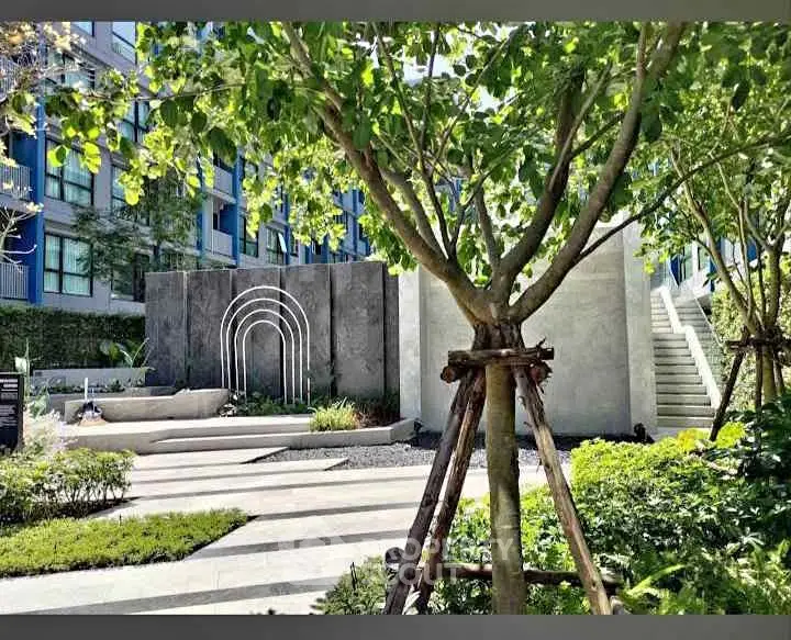 Modern apartment building exterior with landscaped garden and artistic stone feature.