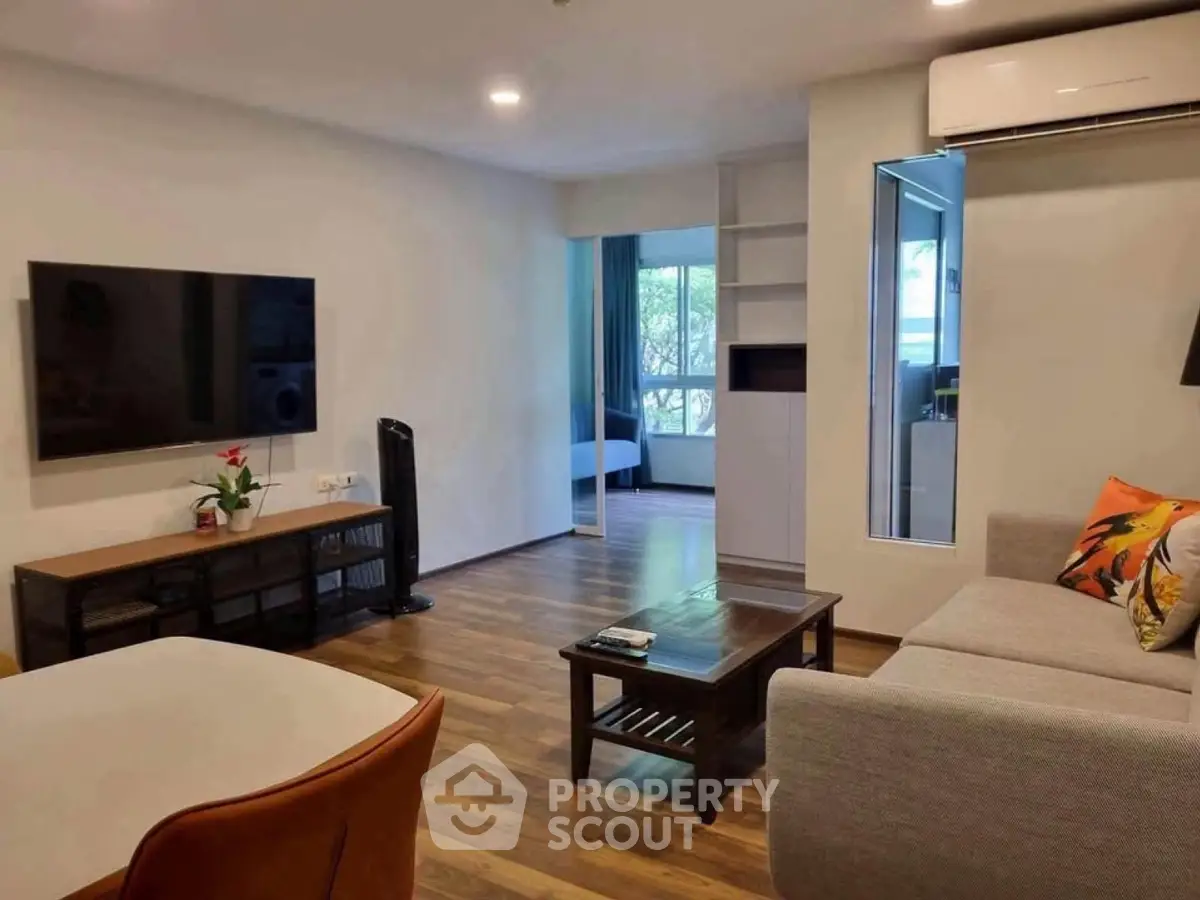 Modern living room with sleek furniture and large TV, featuring a glimpse into a cozy bedroom.