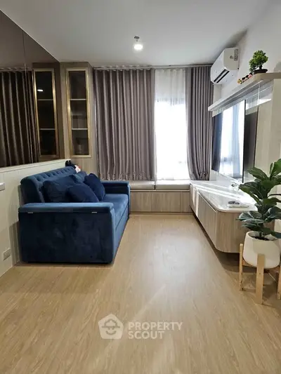 Modern living room with blue sofa, wooden flooring, and large window with curtains.