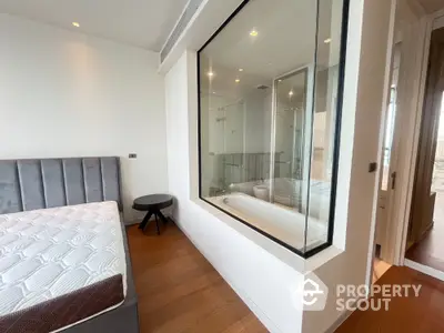 Modern bedroom with glass wall overlooking luxurious bathroom and hardwood floors.