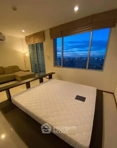 Spacious bedroom with large windows offering stunning city views at dusk.