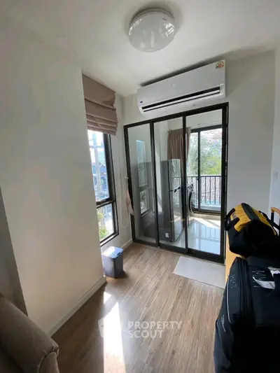 Bright room with air conditioning and balcony access, featuring modern wood flooring and natural light.