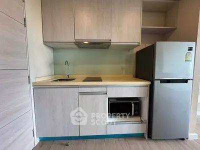 Modern compact kitchen with sleek cabinetry, built-in microwave, and stainless steel fridge.