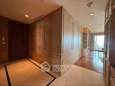 Spacious hallway leading to a bright living area with wooden flooring and elegant paneling.