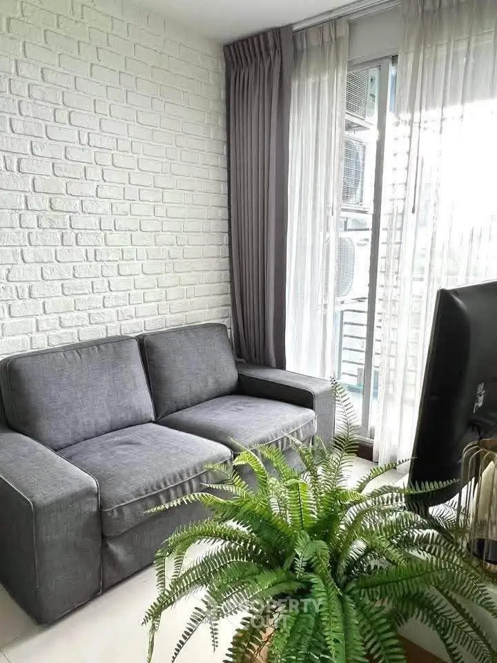 Chic living room with modern gray sofa, white brick wall, and lush green plant near a large window.