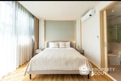 Spacious bedroom with hardwood floors, large bed, and abundant natural light from floor-to-ceiling windows, adjacent to a modern en-suite bathroom.