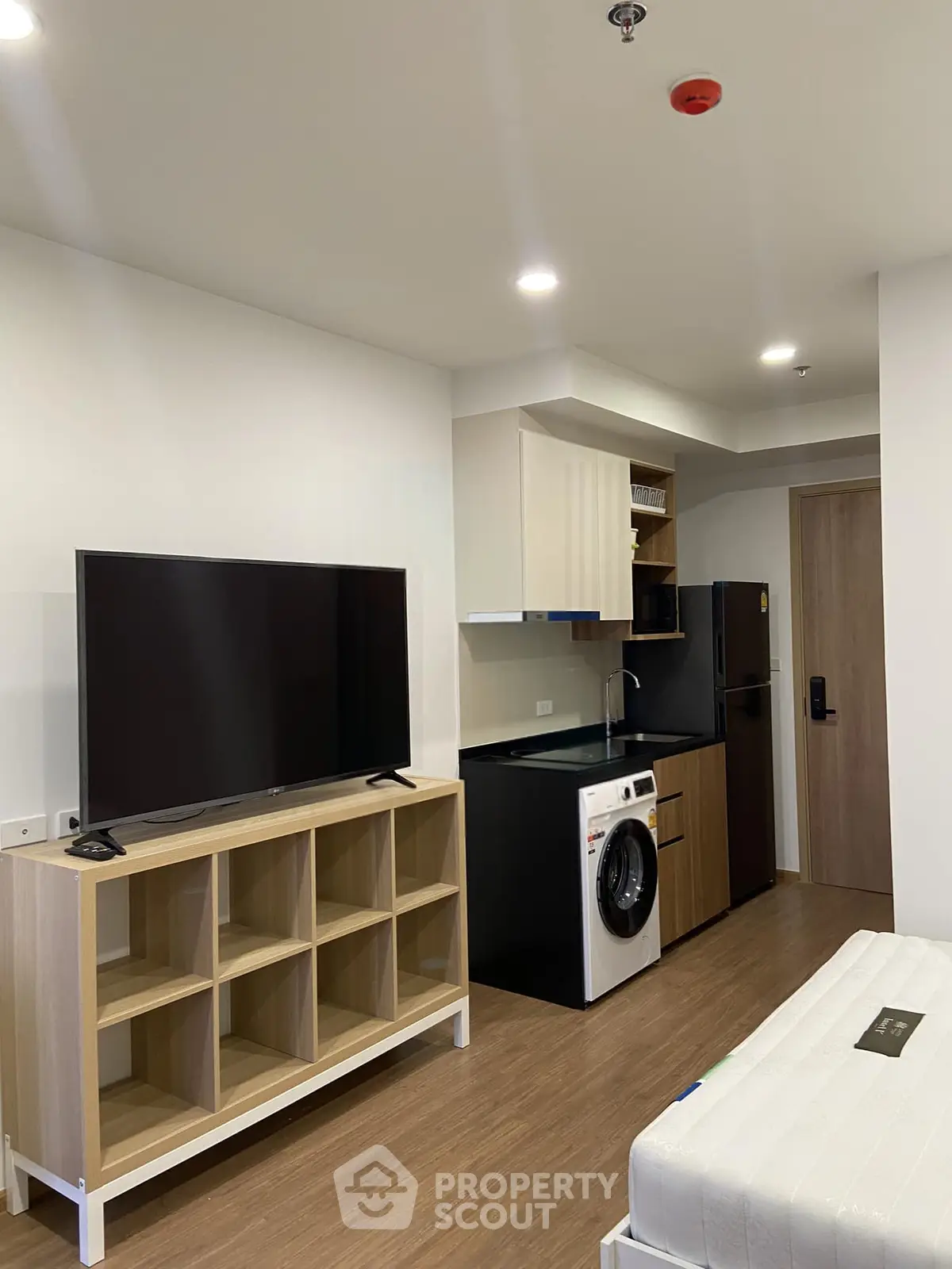 Modern studio apartment with compact kitchen and washing machine, featuring a sleek TV setup and cozy living space.