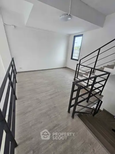 Modern loft space with sleek staircase and large window, perfect for urban living.
