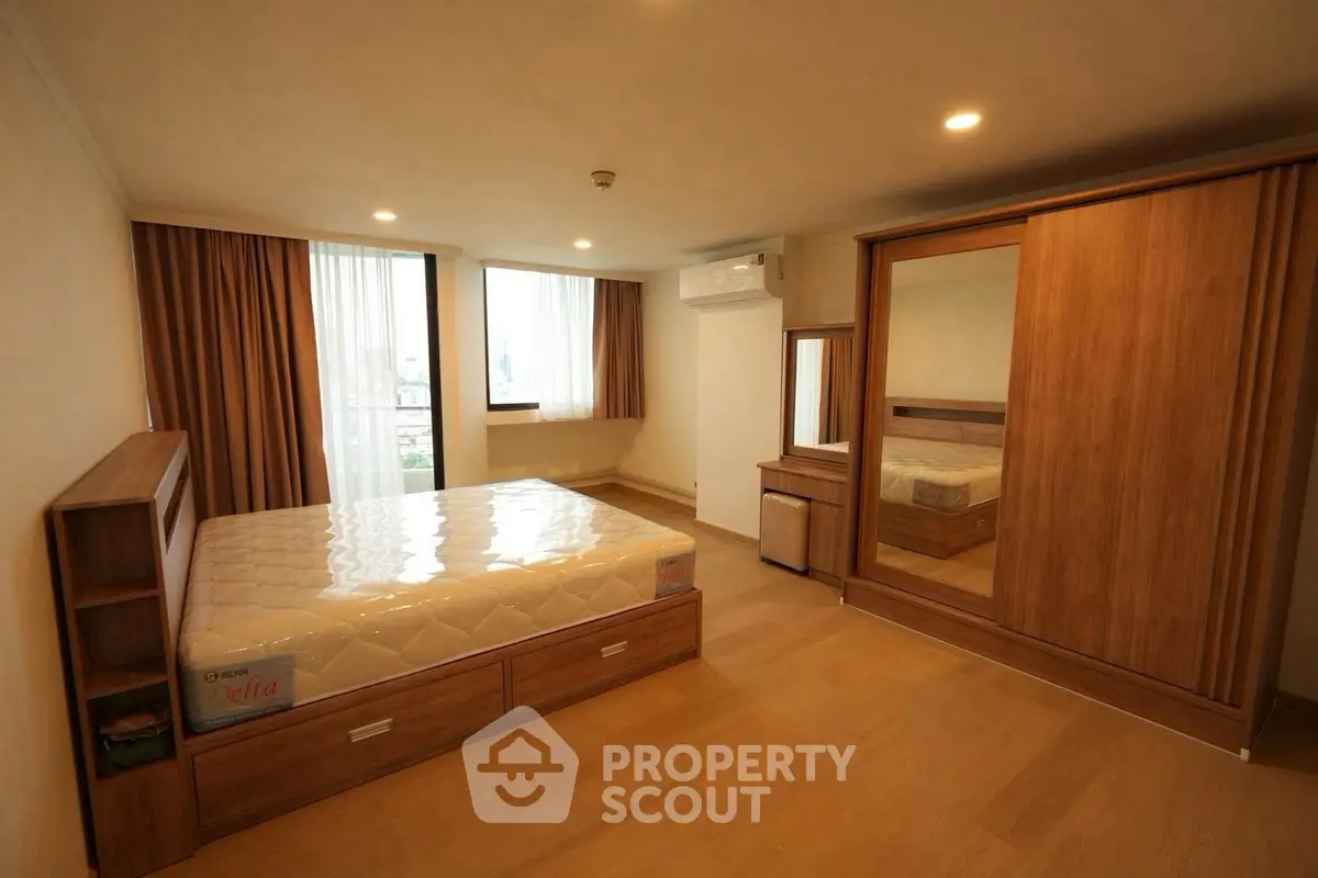 Spacious bedroom with wooden furniture and large windows in modern apartment