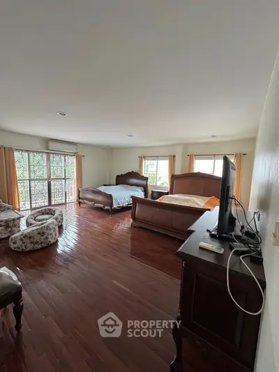 Spacious bedroom with elegant wooden flooring and large windows for natural light.