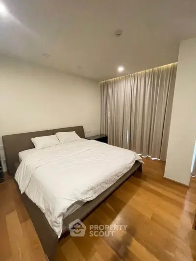 Spacious bedroom with wooden flooring and elegant curtains