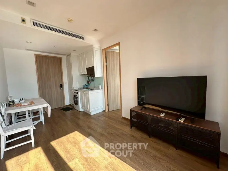 Modern living room with wooden flooring, TV setup, and compact kitchen area.