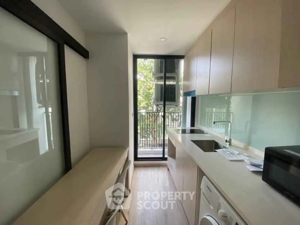 Modern kitchen with sleek cabinetry and balcony view, featuring washing machine and microwave.