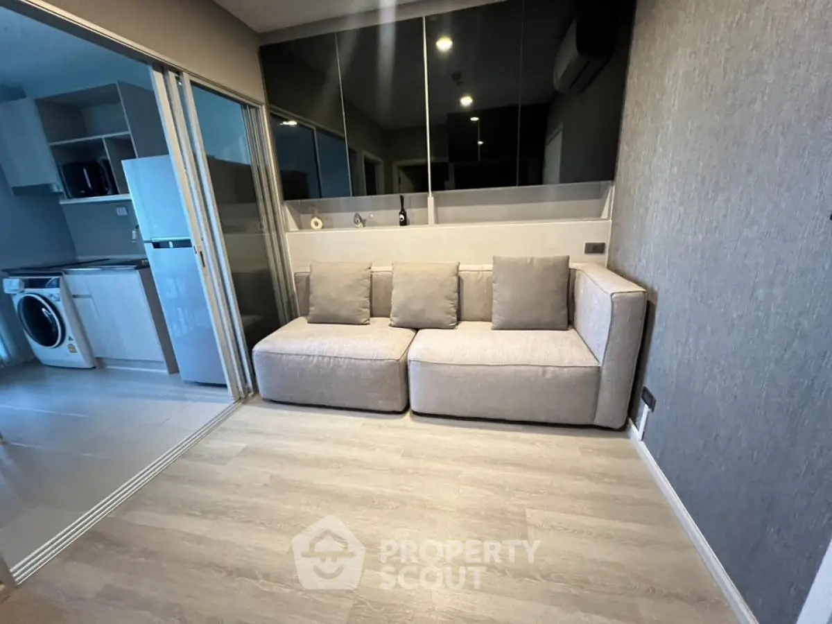 Modern living room with sleek sofa and adjacent kitchen featuring washing machine