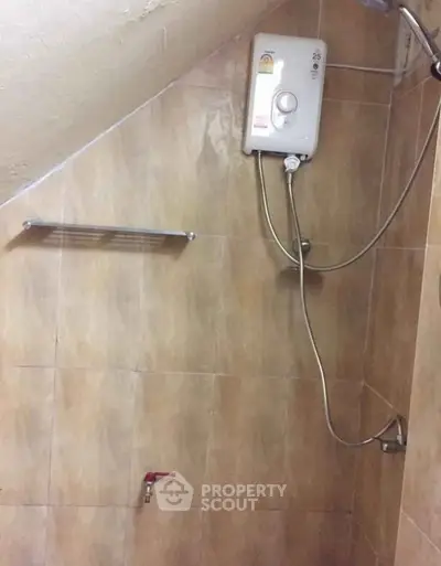 Compact bathroom with electric water heater and tiled walls.