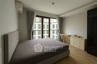 Spacious modern bedroom with large window and minimalist decor in urban apartment.