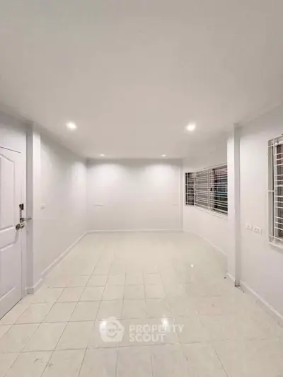 Spacious empty room with tiled flooring and large windows, perfect for customization.