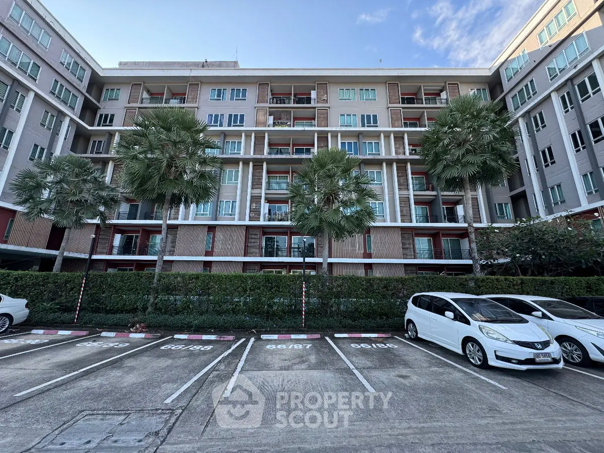 Modern apartment building with palm trees and parking area in front, showcasing urban living.