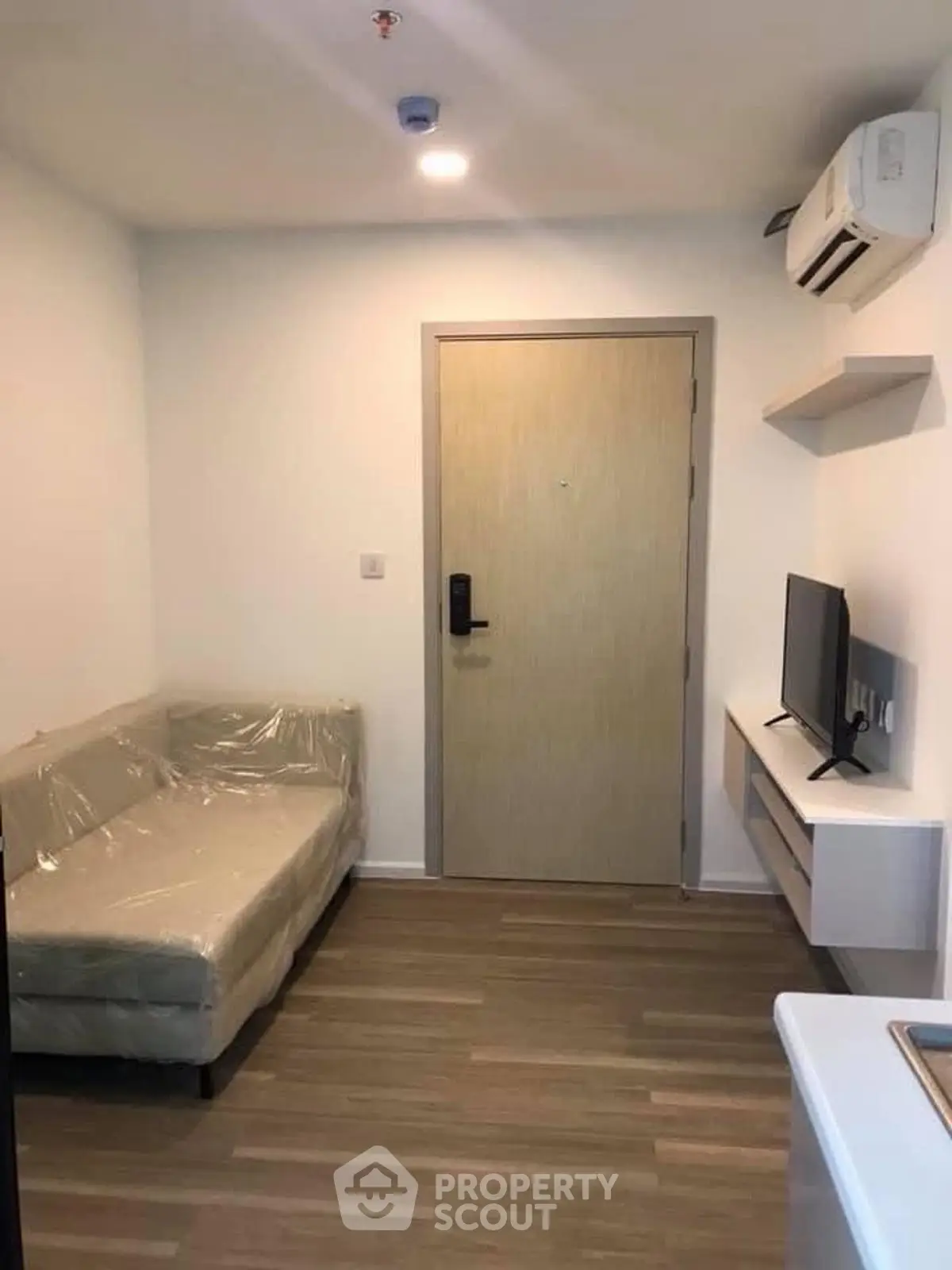 Cozy modern living room with sofa, TV, and air conditioning in a compact apartment.