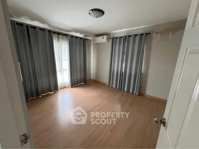 Spacious empty bedroom with wooden flooring and large windows with gray curtains.