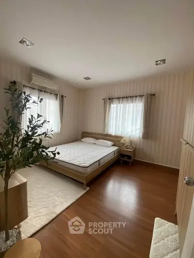 Cozy bedroom with wooden flooring and natural light, featuring a comfortable bed and modern decor.