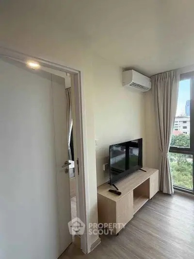 Modern living room with large window and city view, featuring a sleek TV setup and air conditioning.