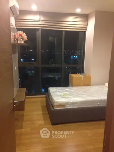 Cozy bedroom with city view, featuring wooden flooring and modern decor.