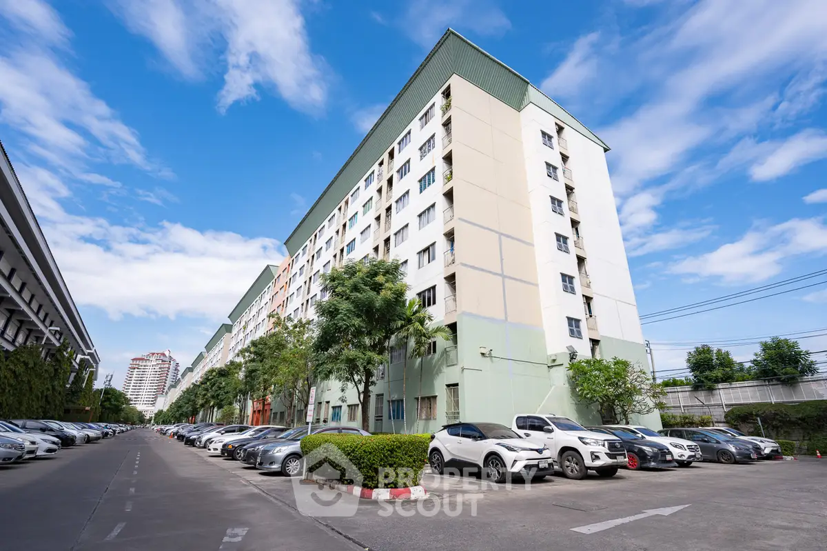 Modern multi-story residential building with parking area and clear blue sky.