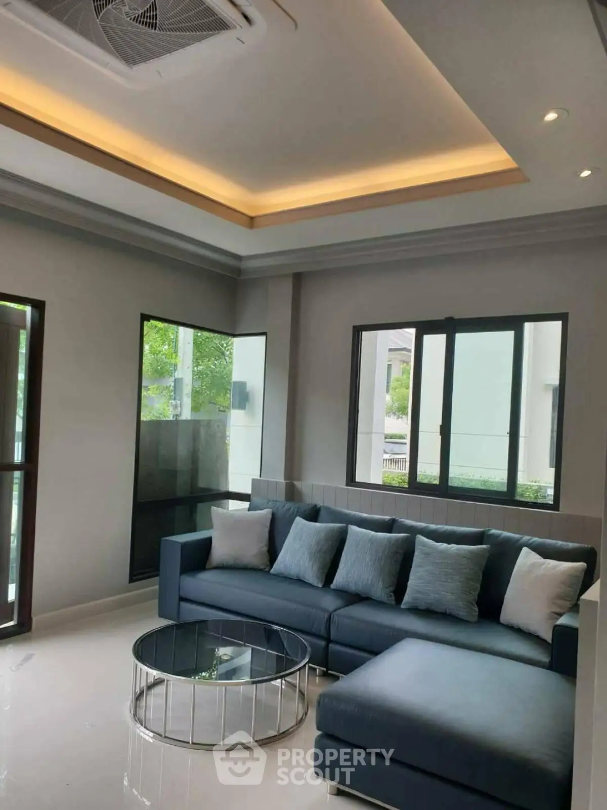 Modern living room with stylish sofa and glass coffee table, featuring large windows and elegant ceiling design.